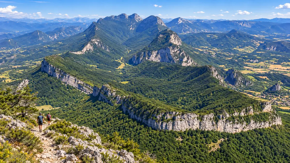 Deux randonneurs sur un sentier rocheux dominent le synclinal boisé de la forêt de Saoû et ses falaises calcaires